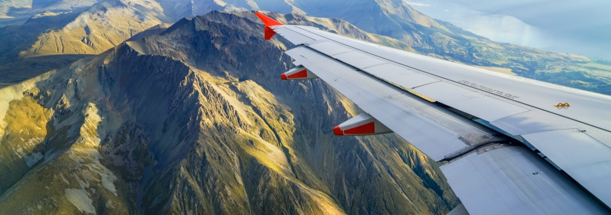 An airplane wing reaches out over a dramatic, mountainous landscape below