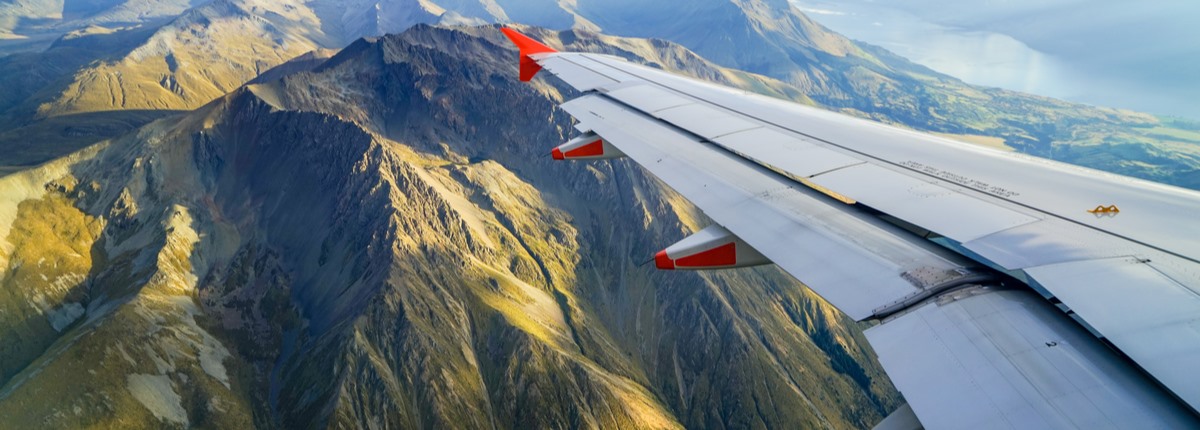 An airplane wing reaches out over a dramatic, mountainous landscape below