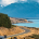 A motor home driving along a winding road beside a lake, with New Zealand's Southern Alps in the background