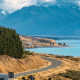 A motor home driving along a winding road beside a lake, with New Zealand's Southern Alps in the background