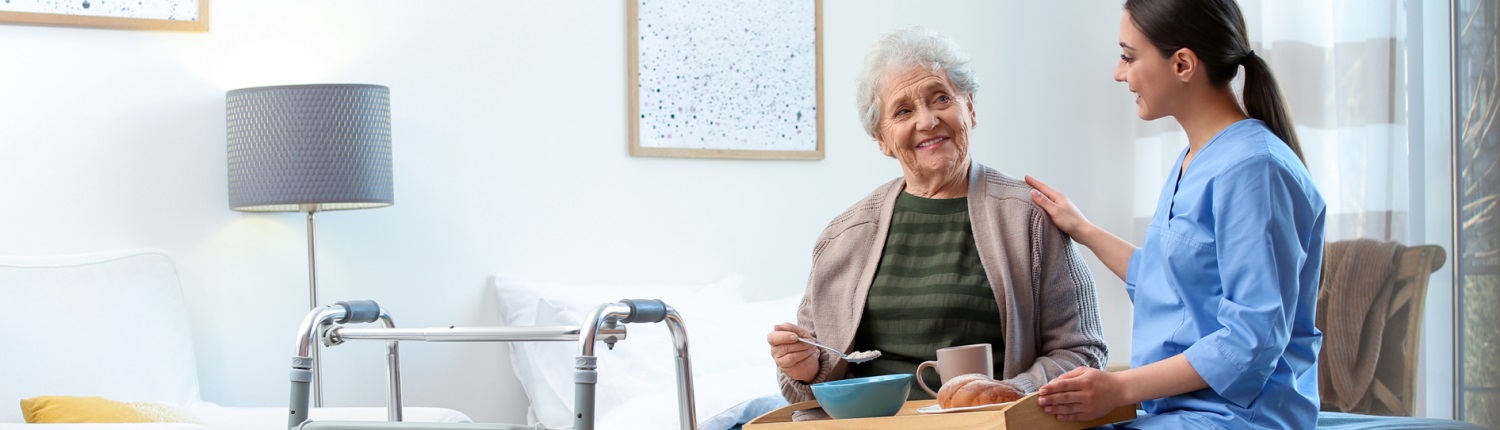 A nurse places a hand on the shoulder of an elderly woman in a care home setting