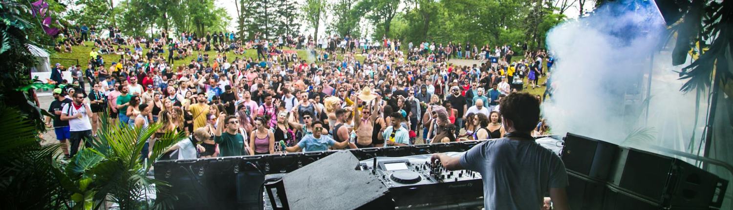 A DJ plays music for a crowd at an intimate outdoor stage at a summer festival